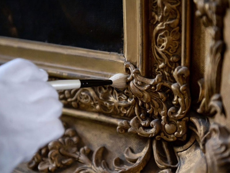 A person wearing a white glove dusting an ornate picture frame.
